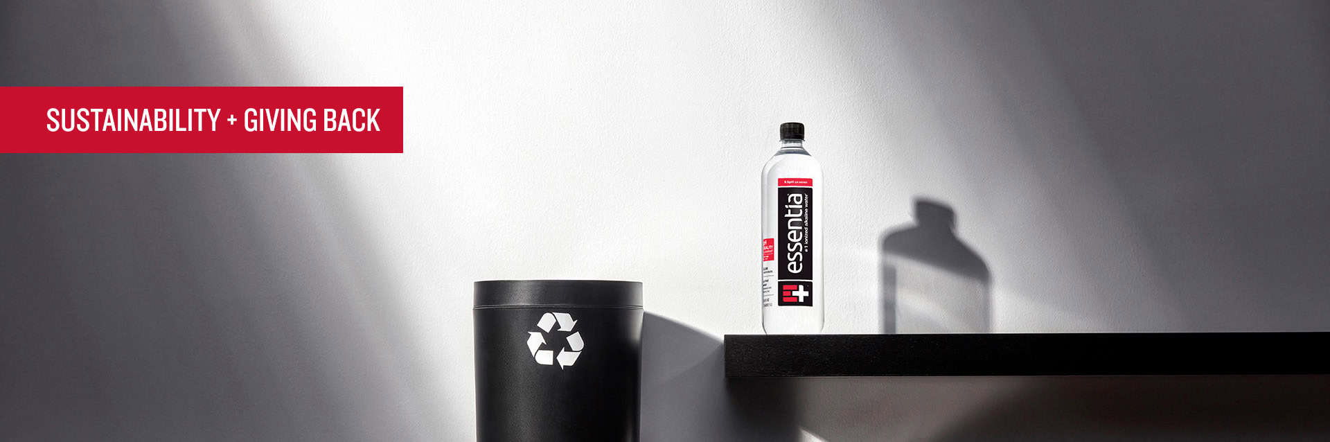 sustainability-header Essentia Water bottle next to Recycling Bin